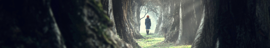 through a corridor of trees, in the distance a lady stands in the light, with her back turned