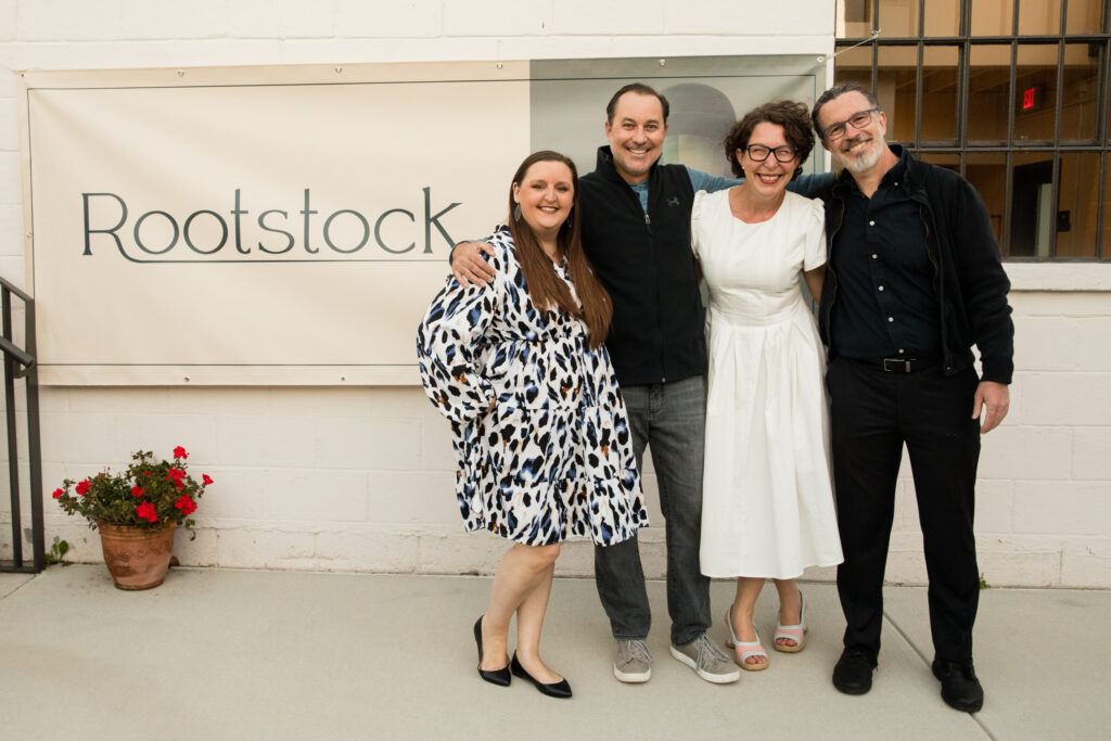 Lindsey, Ryan, Terra, and Tom stand in front of the Rootstock banner prior to the Rootstock launch party.