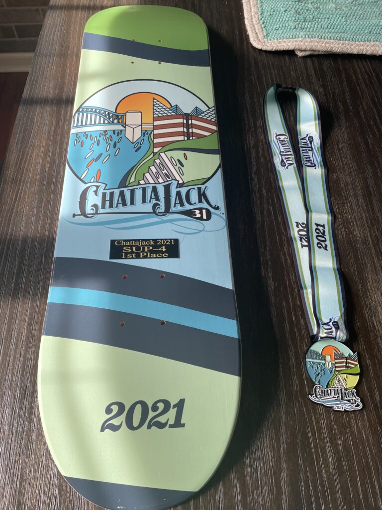 Trophy in the shape of a paddle board with a medal alongside it.