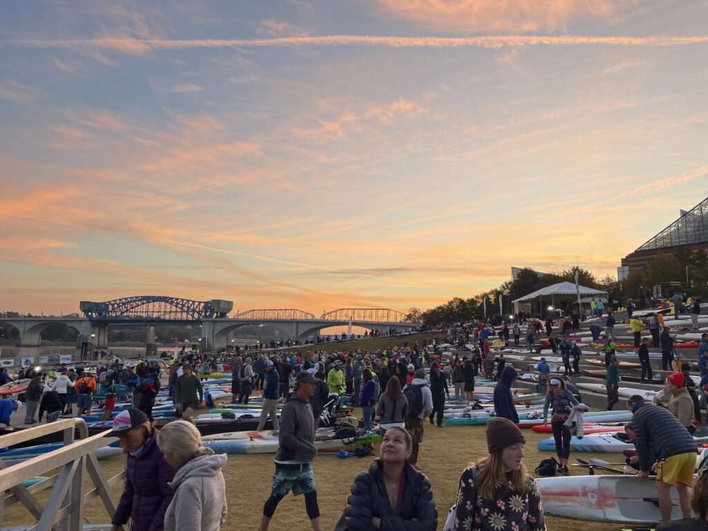 Sunrise over a beach with racers preparing their kayaks and paddle boards.