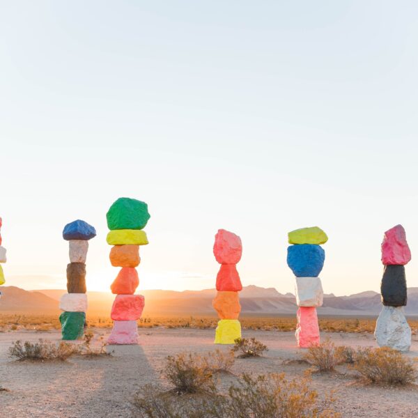 7 brightly painted towers of rocks in a desert.
